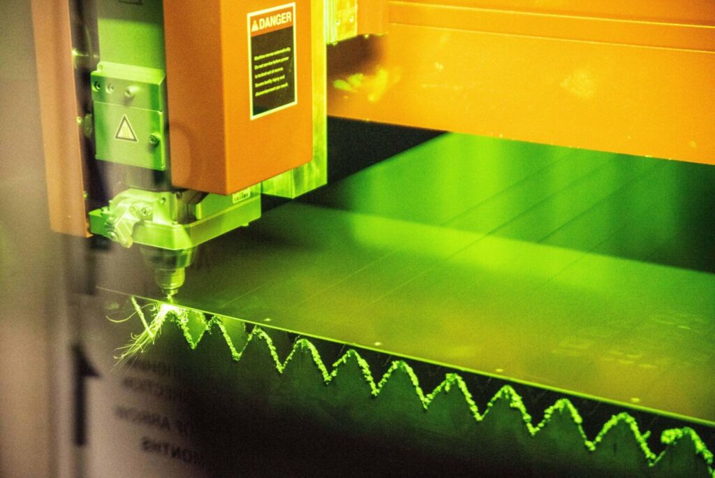 Green laser cutter slicing through aluminum sheet
